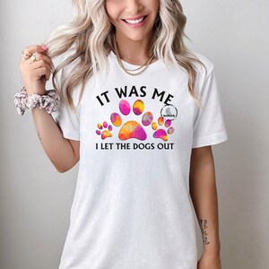 May include: White t-shirt with a colorful paw print design and the text "It was me I let the dogs out".