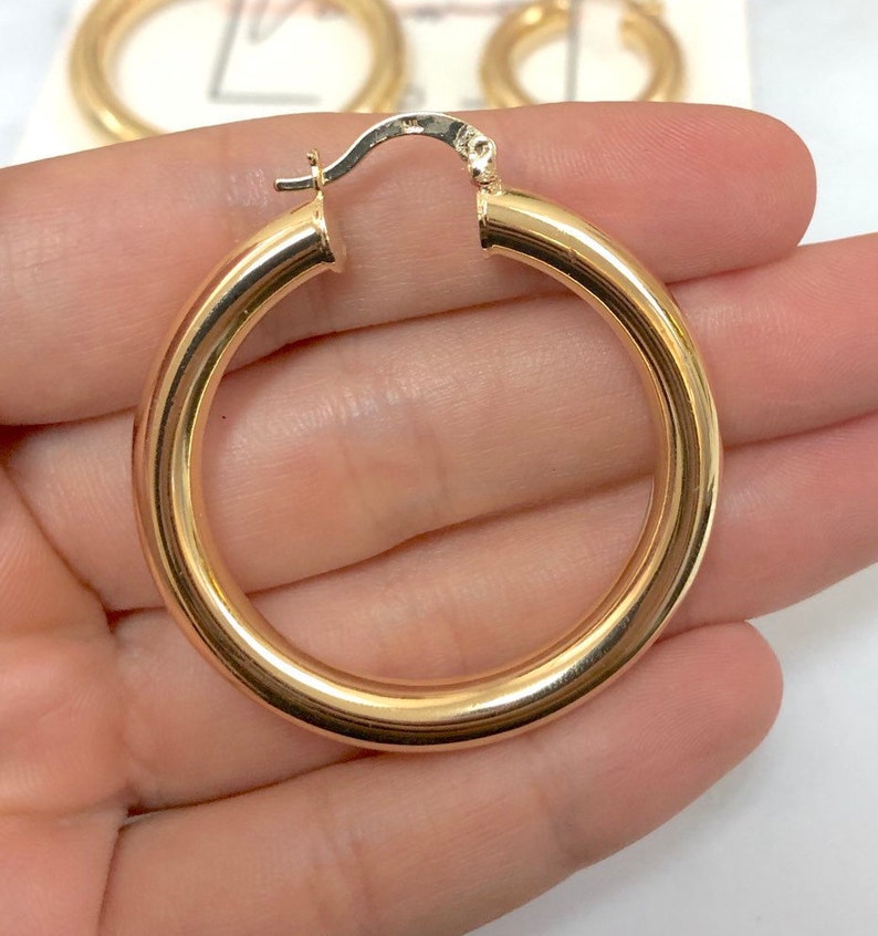 May include: A pair of gold hoop earrings. The earrings are thick and have a smooth finish.