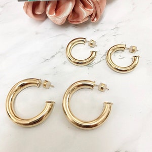 May include: Three pairs of gold hoop earrings of different sizes. The earrings are thick and have a smooth, polished finish.