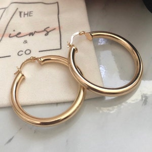 May include: A pair of gold hoop earrings. The earrings are thick and have a smooth finish.