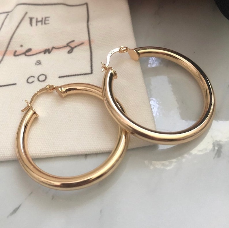 May include: A pair of gold hoop earrings. The earrings are thick and have a smooth finish.
