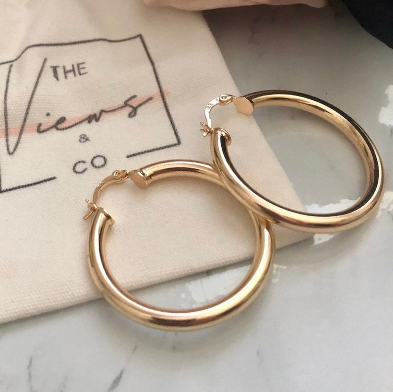 May include: A pair of gold hoop earrings. The earrings are thick and have a smooth, polished finish.