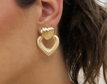 May include: Gold heart-shaped earrings with a textured design. The earrings are dangling and have a heart-shaped loop at the top.