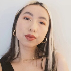 May include: A woman with black and white hair wearing gold hoop earrings and a gold chain necklace. She is wearing a black tank top.