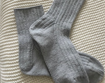 以下が含まれることがあります： 灰色のニットソックスのペア。ソックスは折り畳まれて、白いニットの表面に置かれています