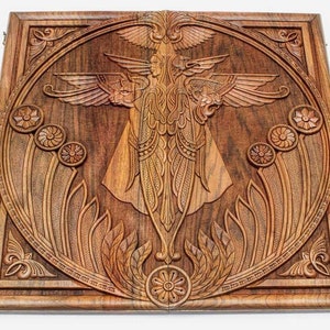 Puede incluir: Un colgante de pared de madera con un diseño tallado de una criatura alada con detalles intrincados. El diseño está rodeado por un marco decorativo.