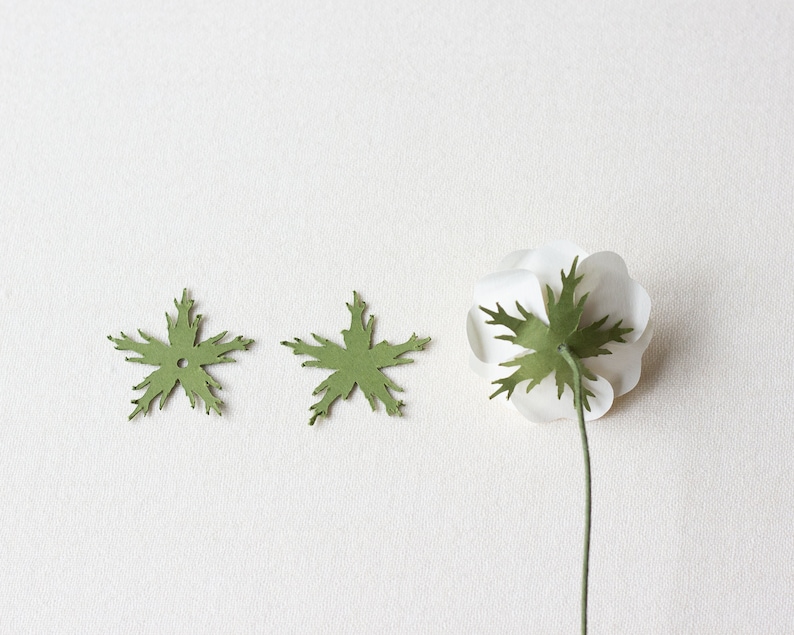 May include: Two green paper leaves with a hole in the center and a white paper flower with a green paper leaf attached to the stem.