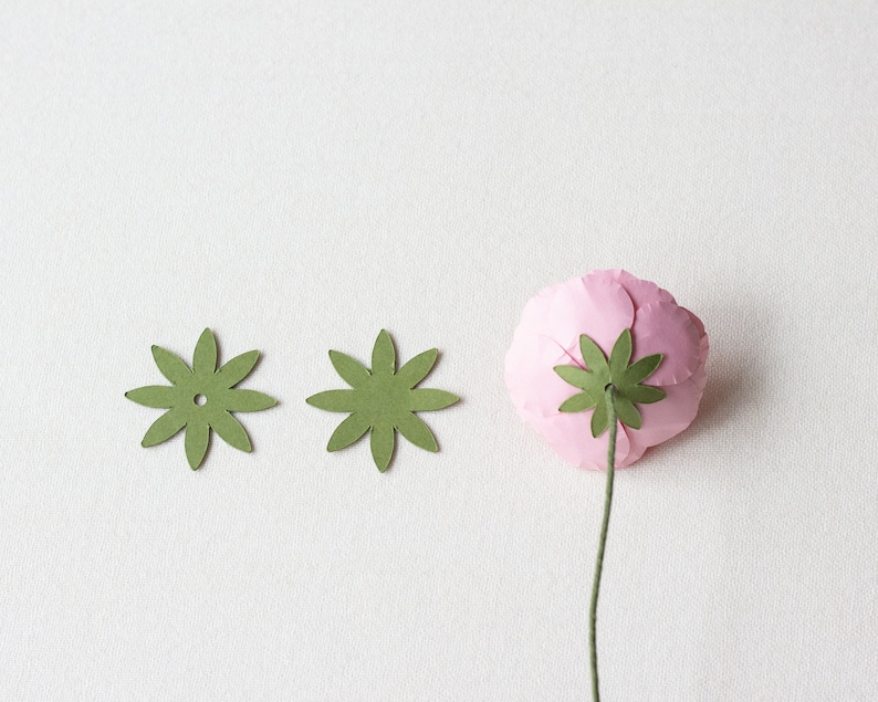 May include: Two green paper flower embellishments with a hole in the center and a pink paper flower with a green paper stem.