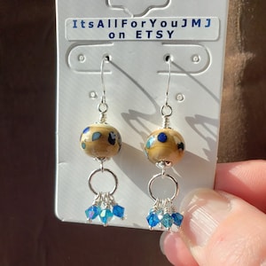Könnte beinhalten: Ein Paar Hängeohrringe mit einer braunen und blauen Perle mit Muster und einem Cluster aus blauen Kristalltropfen. Die Ohrringe befinden sich auf einer weißen Karte mit dem Text "ItsAllForYouJMJ on ETSY".