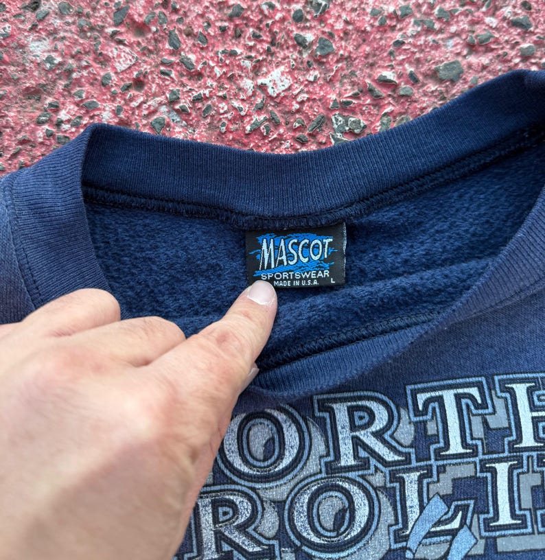 May include: Navy blue sweatshirt with a white graphic print that says "North Carolina" and a small tag that says "Mascot Sportswear Made in U.S.A. L"