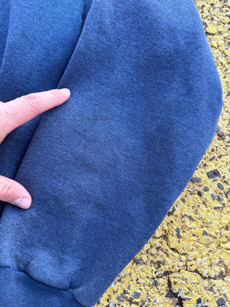 May include: Close-up of the blue fabric of a sweatshirt sleeve. The fabric has a slightly textured appearance.