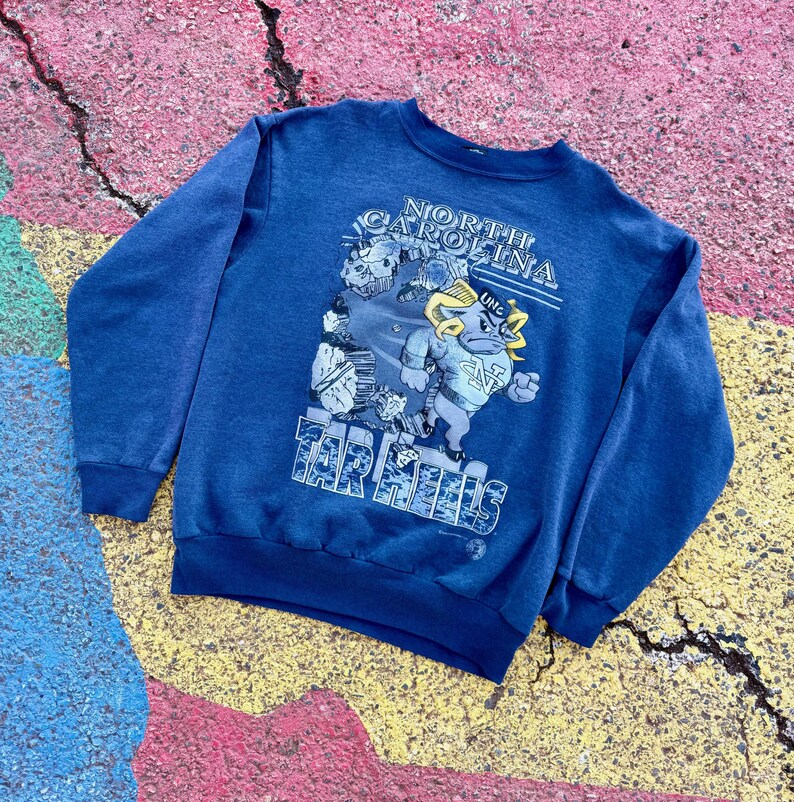 May include: A blue sweatshirt with a graphic of the University of North Carolina Tar Heels mascot, a ram, with the text "North Carolina Tar Heels" and "UNC" printed on the front.