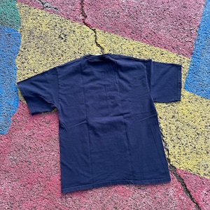Peut inclure: Un t-shirt bleu marine &agrave; manches courtes, pos&eacute; &agrave; plat. Le t-shirt est fait d'une mati&egrave;re douce. Le fond est une surface color&eacute;e et textur&eacute;e avec des taches roses, jaunes, bleues et vertes.