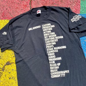 May include: Black t-shirt with white text listing various production roles, including casting, directing, and comedy. Features the Nike logo and "The Cosby Show" logo. A vintage tee.
