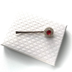 May include: A gold hair clip with a red rhinestone in the centre surrounded by clear rhinestones.