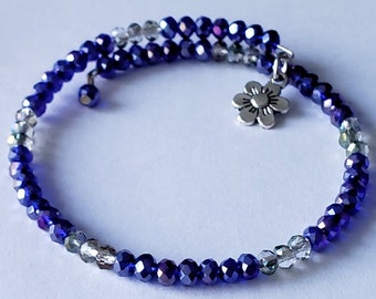 May include: A blue and clear crystal beaded bracelet with a silver flower charm. The bracelet is wrapped twice around the wrist.