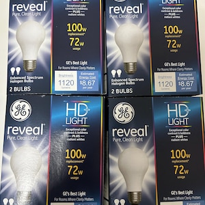 May include: Four boxes of GE Reveal HD Light bulbs. Each box features a white light bulb image, the text "reveal Pure, Clean Light", and details about brightness and energy usage. The boxes are primarily navy blue with colorful accents.