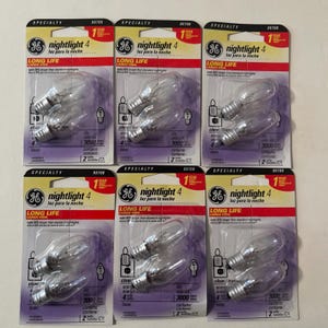 May include: Six packages of GE nightlight 4 bulbs. Each package contains two clear bulbs with a long-life design. The packaging is white, red, and purple with the text "nightlight 4" and "LONG LIFE".