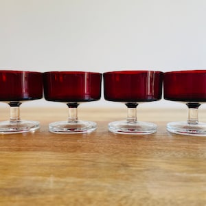 May include: Set of four clear glass stemmed dessert cups with a deep red coloured bowl. The cups are arranged in a row on a wooden surface.