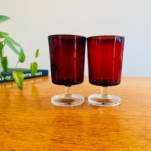 Peut inclure: Deux verres à boire assortis dotés de bols rouge rubis profond aux parois droites. Chaque verre est soutenu par un pied court en verre transparent et une base circulaire en verre transparent, offrant une assise stable au récipient coloré.