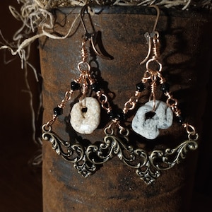 May include: A pair of dangle earrings with a white and gray stone, black beads, and copper wire. The earrings are attached to a bronze filigree design.