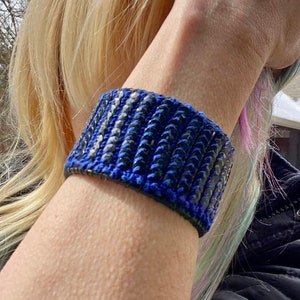 May include: A blue and black beaded bracelet with a woven design. The bracelet is made of small, round beads that are sewn together in a pattern.