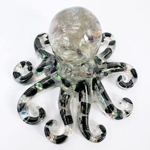 May include: A clear resin octopus sculpture with black and white patterned tentacles. The head is filled with clear resin and small, colorful objects. The sculpture is a decorative item, suitable for home decor.