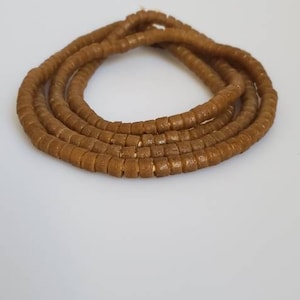 May include: A long strand of brown beads made of small, square-shaped pieces. The beads are arranged in a circular shape, creating a necklace or bracelet.
