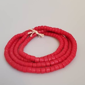 May include: A strand of bright red beads, made of a smooth, rounded material. The beads are strung together on a thin, white cord.