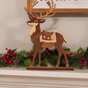 May include: A handcrafted wooden reindeer figurine with detailed antlers and a saddle. The reindeer is brown with lighter accents and stands on a wooden base. The image also includes a decorative garland with red berries and greenery, and a sign that says "handcrafted Wood Art".