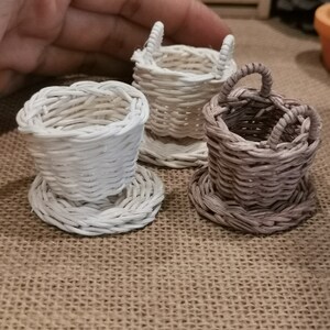 May include: Three miniature woven baskets, one white, one brown, and one white with a brown base. The baskets are made of woven paper and have a handle.