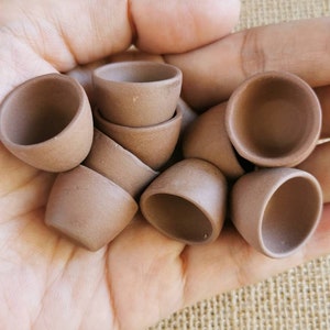 Peut inclure: Une collection de petites tasses en céramique brune, empilées et disposées dans une main. Les tasses sont non vernissées et ont un aspect rustique et terreux.