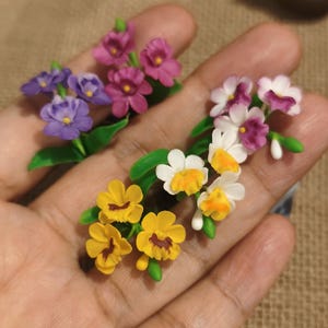 Puede incluir: Dos racimos florales en miniatura con pequeñas flores esculpidas en tonos morado, magenta, blanco y amarillo. Cada racimo incluye hojas y tallos verdes, con las flores moradas y magenta agrupadas y las flores blancas y amarillas dispuestas en un conjunto separado.