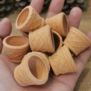 Könnte beinhalten: Eine Sammlung von acht kleinen, terracottafarbenen, kegelförmigen Pflanzgefäßen mit einer Waffelstruktur. Die Pflanzgefäße sind in einer Hand angeordnet.