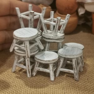 May include: A set of six white wooden stools with a distressed finish. The stools are stacked and arranged in a pyramid shape.