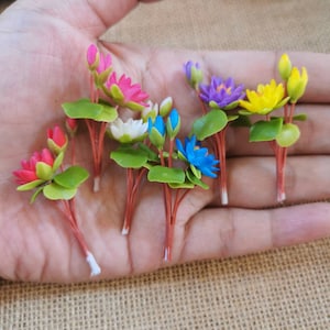 Puede incluir: Surtido de flores de nenúfar artificiales en miniatura de varios colores, incluyendo rosa, amarillo, azul, blanco y morado. Cada flor tiene hojas verdes y un tallo marrón.
