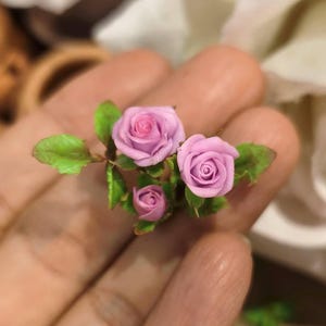 Peut inclure: Un petit bouquet de roses roses avec des feuilles vertes. Les roses présentent un design de pétales délicat et superposé, et les feuilles sont détaillées avec des nervures visibles. L'ensemble est un petit arrangement floral artisanal.