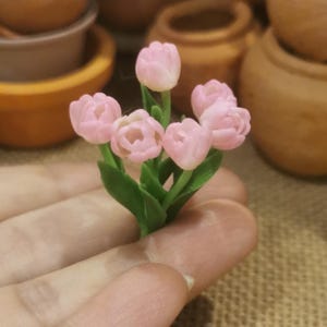 May include: A bouquet of pink miniature tulips with green stems and leaves. The tulips are made of polymer clay and are perfect for dollhouses or miniature gardens.