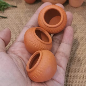 May include: Three small terracotta pots with a textured surface. The pots are unglazed and have a natural brown colour.