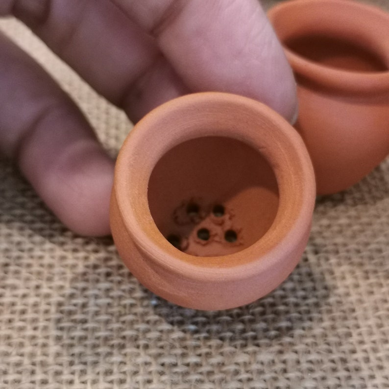 K&ouml;nnte beinhalten: Ein Terrakotta-Topf mit Abzugsl&ouml;chern im Boden. Der Topf ist klein und hat eine abgerundete Form.