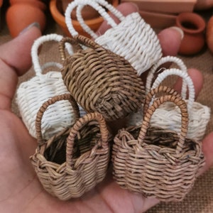Puede incluir: Una colección de cestas tejidas en miniatura en varios tonos de marrón y blanco. Cada cesta tiene un asa pequeña, y el patrón de tejido es visible. Las cestas son probablemente para fines decorativos o para objetos pequeños.