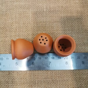 K&ouml;nnte beinhalten: Drei kleine Terrakottat&ouml;pfe, zwei mit Abzugsl&ouml;chern und einer ohne, auf einem Lineal ausgerichtet. Die T&ouml;pfe haben einen Durchmesser von etwa 4 cm.
