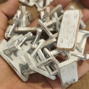 Può includere: Una collezione di tavoli in miniatura in legno con una finitura in vernice bianca invecchiata. Ogni piccolo tavolo presenta un piano rettangolare e quattro gambe, con venature del legno e bordi usurati visibili su tutti i pezzi.