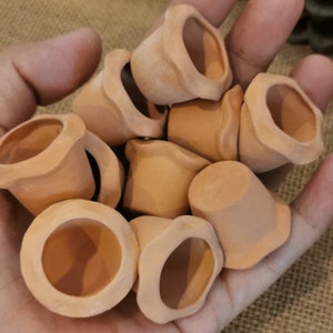Puede incluir: Un conjunto de pequeñas macetas de terracota sin esmaltar. Las macetas tienen forma redondeada con un borde acampanado y festoneado. El color terracota es un tono cálido y terroso. Estas macetas en miniatura son probablemente para plantas pequeñas o fines decorativos.