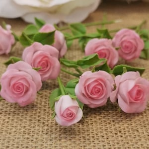 Puede incluir: Un conjunto de ocho rosas artificiales de color rosa con hojas y tallos verdes. Las rosas están dispuestas sobre una superficie de arpillera marrón.