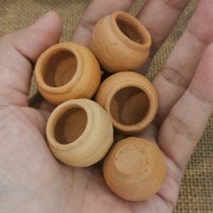May include: Five small terracotta pots, unglazed, with rounded bottoms and slightly flared rims. The pots are arranged in a hand, with the largest pot at the top and the smallest pot at the bottom.
