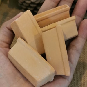Pode incluir: Quatro pequenos vasos retangulares de terracota, empilhados uns sobre os outros, em uma mão.