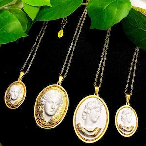 以下が含まれることがあります： 白いカメオ風の女性の肖像画が描かれた楕円形のペンダントがついた、金色のチェーンネックレスが4本。ペンダントには金色のアクセントが施され、黒い背景に飾られています。