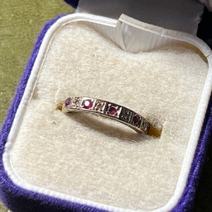 May include: A delicate silver band ring with a row of small red gemstones and smaller clear gemstones set in a milgrain design.