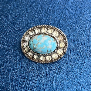 May include: A turquoise cabochon stone set in a silver oval ring with clear rhinestones around the edge.